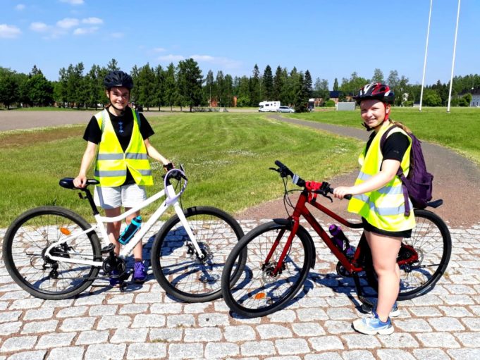Kaksi nuorta poseeraavat hymyillen pyörien kanssa kameralle